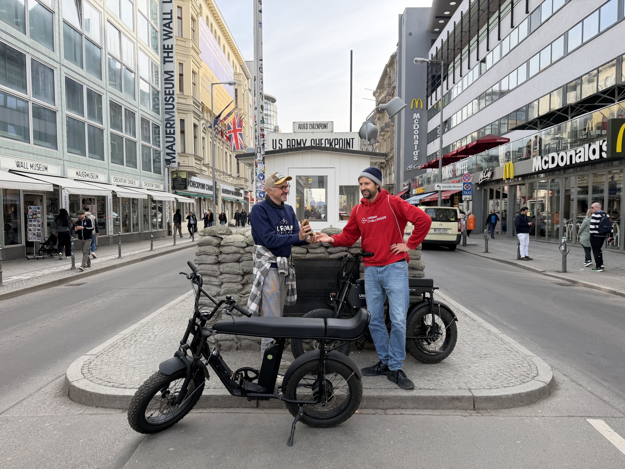 2 personen posieren vor dem checkpoint charlie mit einem e-cruiser