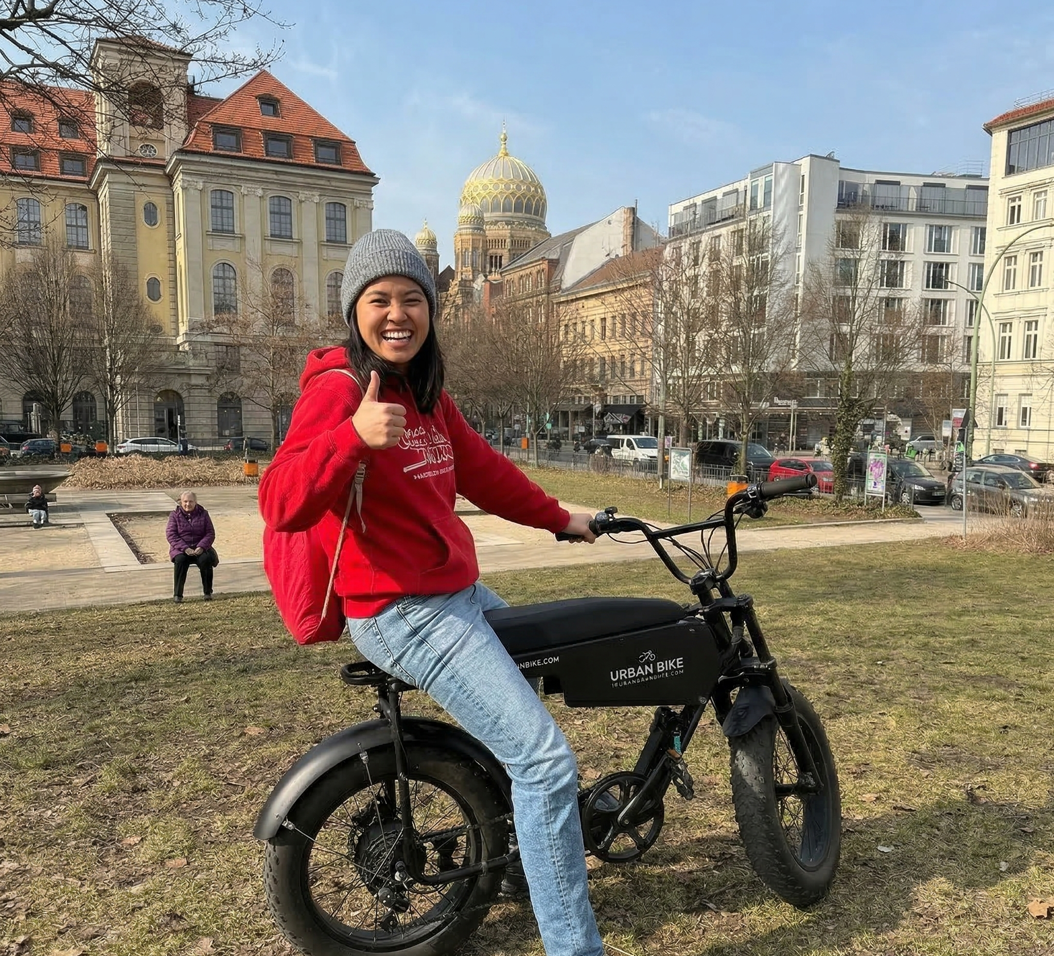 Person sitzt auf E-Cruiser, Daumen hoch im Hintergrund sehen wir das ehemalige Telegrafenamt udn die neue Synagoge